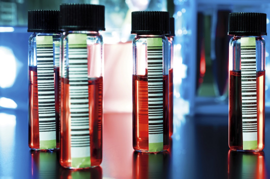 Des flacons de médicaments contenant un liquide rouge sont posés sur une table.