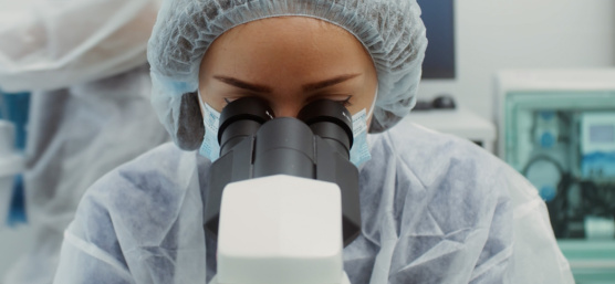Une personne vêtue d'une combinaison de protection regarde à travers un microscope