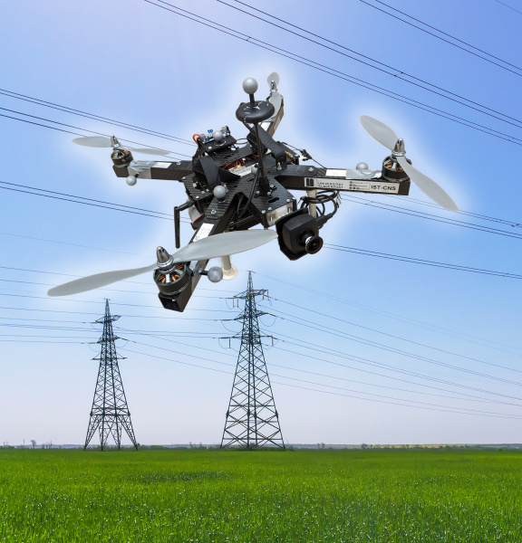 Un drone équipé d'une caméra IDS plane devant des lignes et des pylônes électriques.