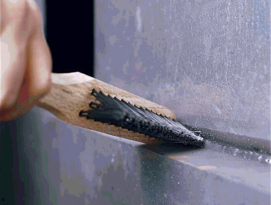 Main qui nettoie les cordons de soudure ou les surfaces métalliques avec une brosse métallique