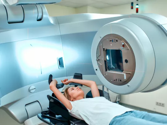 Une femme est allongée sur un divan médical devant un appareil de radiothérapie.