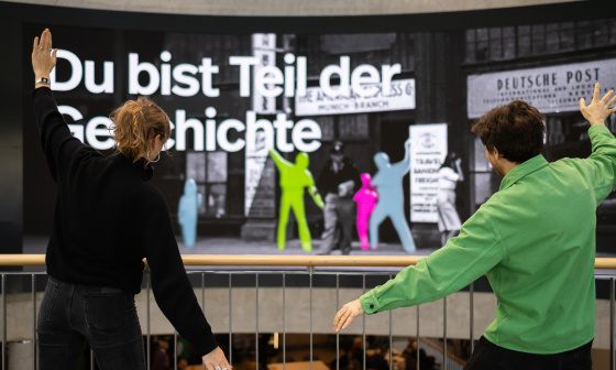 Deux personnes posent devant un grand écran interactif sur lequel apparaissent des silhouettes colorées