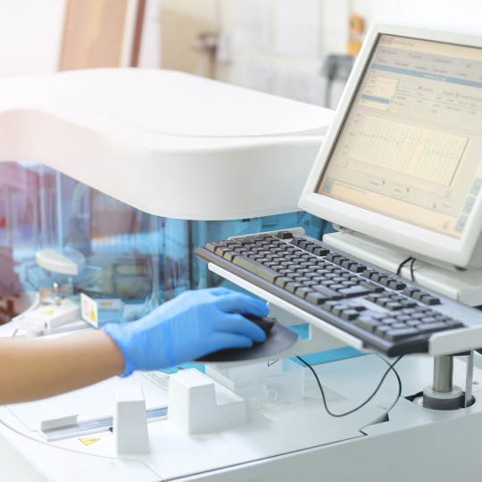 Ordinateur dans un laboratoire, utilisé par une personne portant un gant bleu.