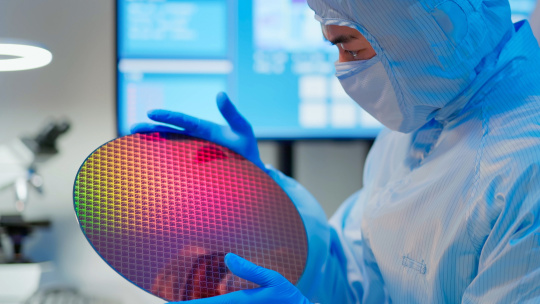Un homme en costume bleu examine une carte à circuit imprimé ronde dans un laboratoire.