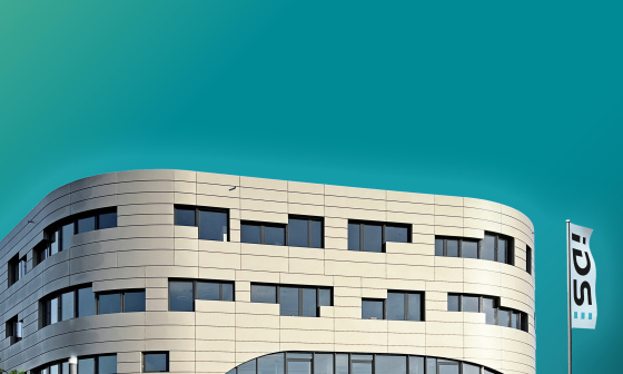 Vue frontale du bâtiment principal d'IDS avec un drapeau sur fond de ciel aux couleurs de l'entreprise.