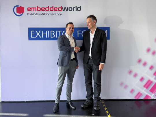 2 directeurs généraux se serrent la main devant un stand du salon Embedded World