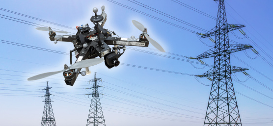 Un drone équipé d'une caméra IDS plane devant des lignes et des pylônes électriques.