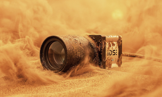 Caméra industrielle à moitié enfouie dans le sable, entourée de nuages de sable soulevés.