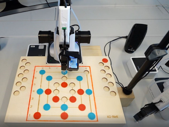 Bras de robot avec caméra devant le plateau de jeu du moulin