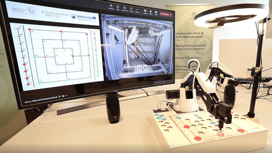 Le robot joue au moulin sur le plateau de jeu et est éclairé par une lampe, à côté de l'écran.
