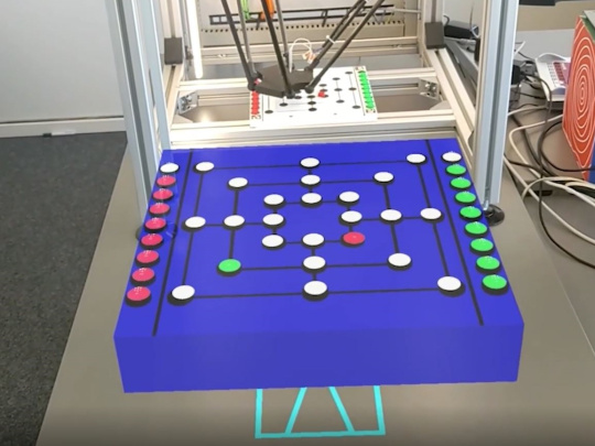 Le robot joue au moulin dans la boîte, devant la boîte le plateau de jeu équivalent pour jouer contre le robot.