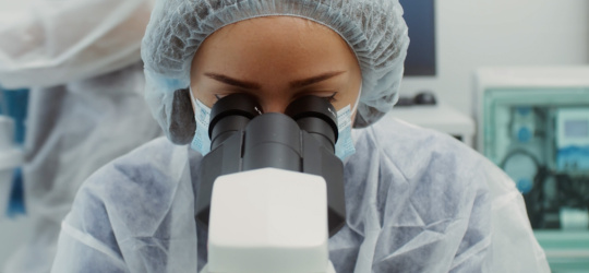 Une femme portant des vêtements de protection regarde dans un microscope.