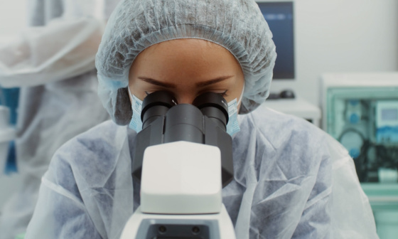 Une personne vêtue d'une combinaison de protection regarde à travers un microscope