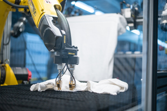 Un robot jaune déployant une serviette dans une blanchisserie industrielle.
